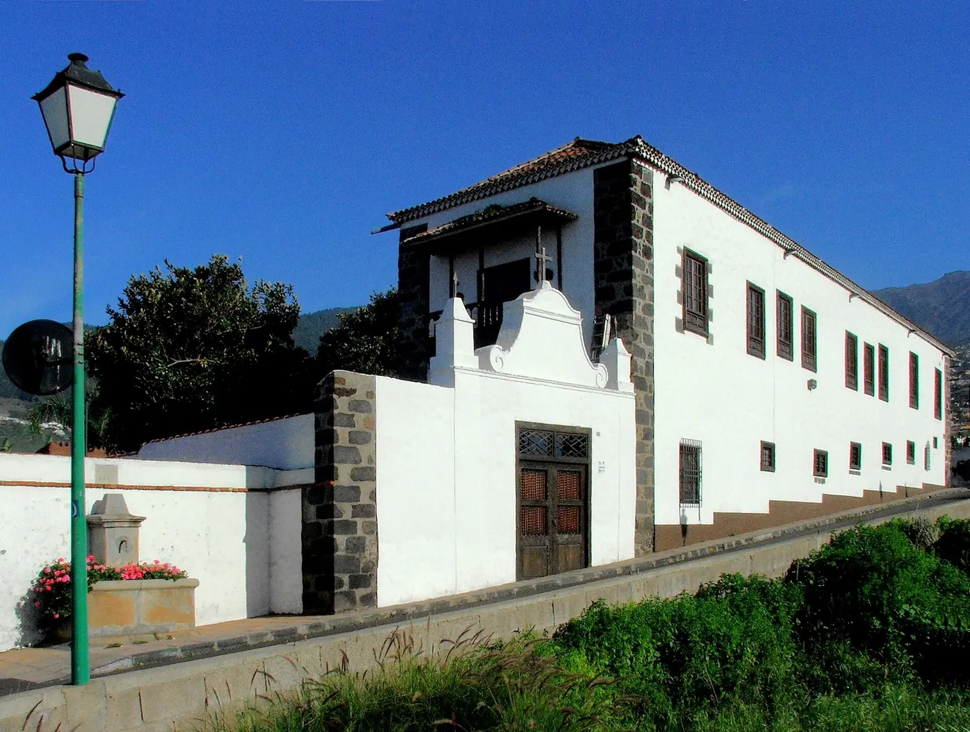 El frontón y la puerta de madera del muro de entrada de la Casa Ábaco, con un balcón de madera encima y montañas verdes al fondo